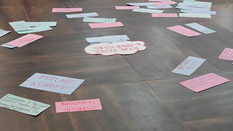 Scattered across the floor are various colourful cards featuring terms and ideas such as ‘Informal Economy’, ‘Future & Change’ and ‘Natural Injustice’.