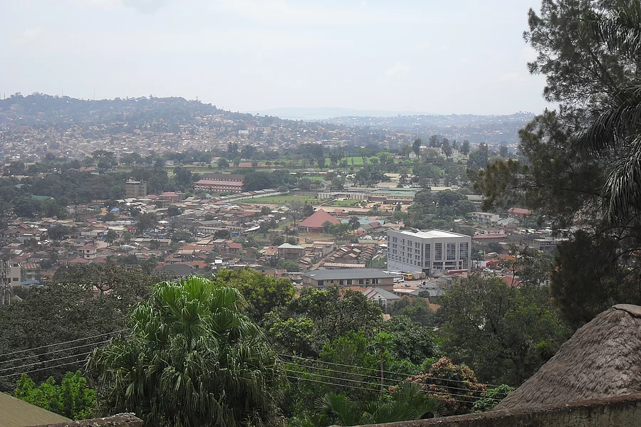 A panoramic photograph shows the city of Kampala, the capital of Uganda, with green trees in the foreground.